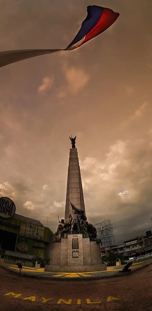 The Bonifacio Monument in Metro Manila beneath a Philippine flag.