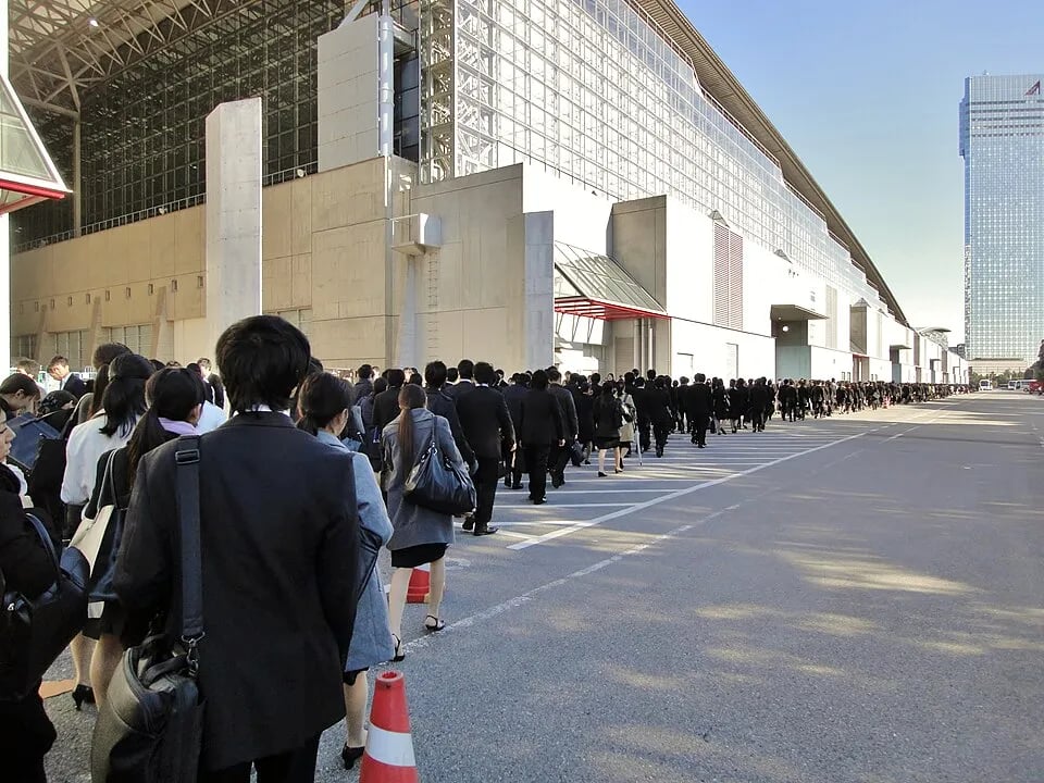 Job seekers in dark recruitment suits wait in a line in Japan.