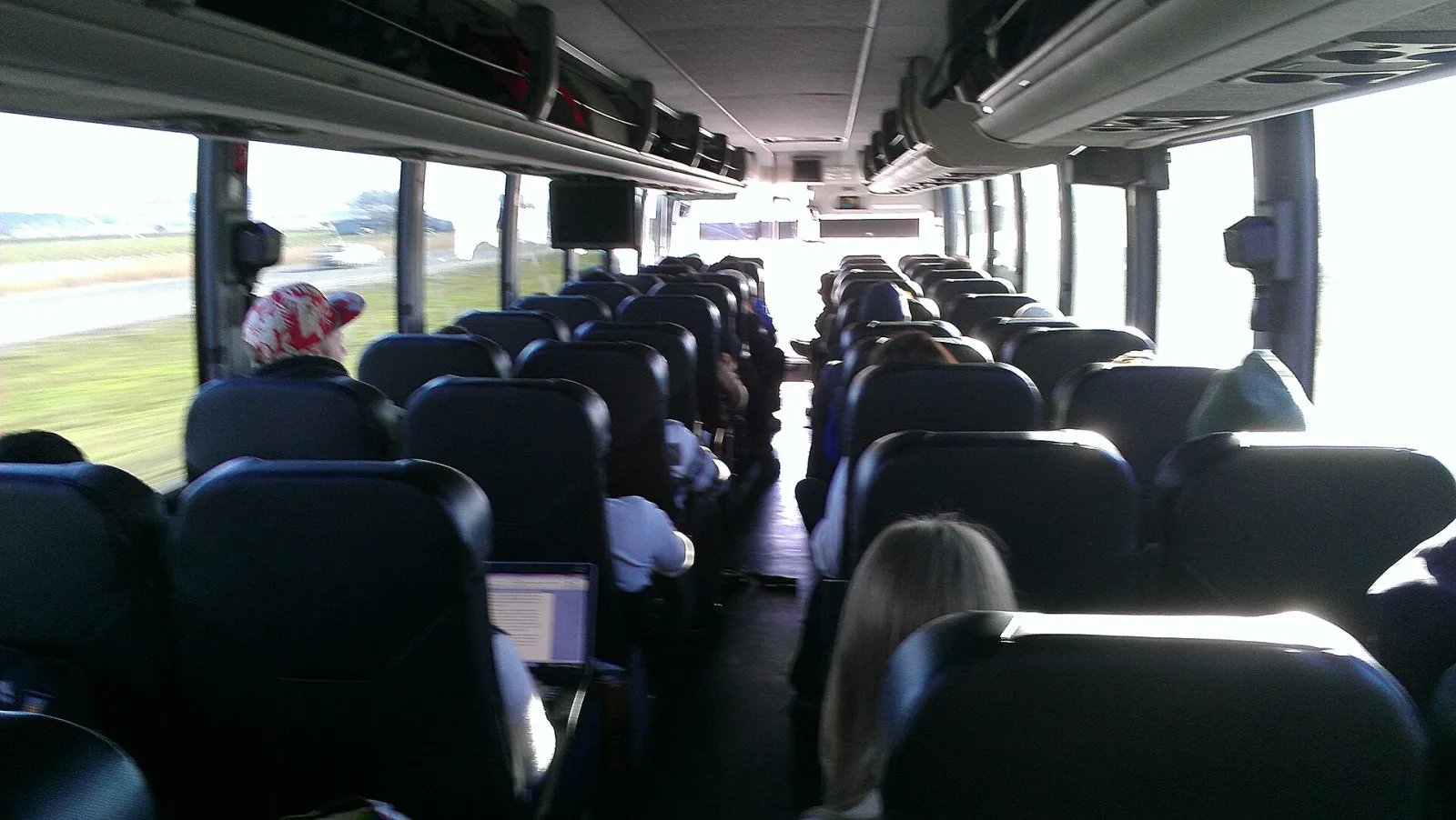 View down the aisle of a long-distance bus, with empty seats on both sides and soft light from the windows.