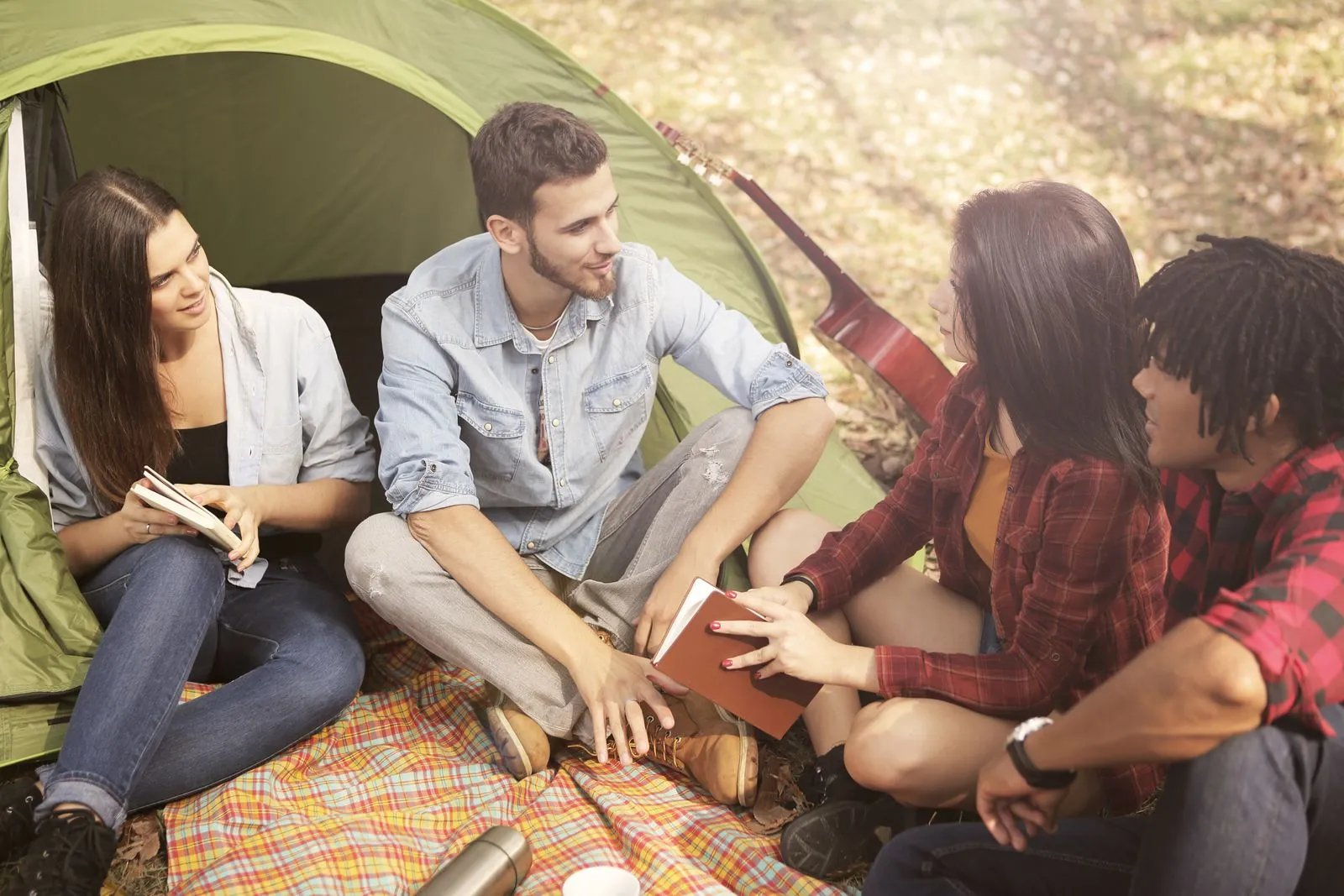 Friends sitting on the grass by a tent on a sunny day, talking and relaxing outdoors.