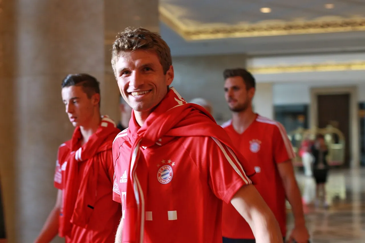 Thomas Müller smiles while wearing the red kit of Bayern Munich.