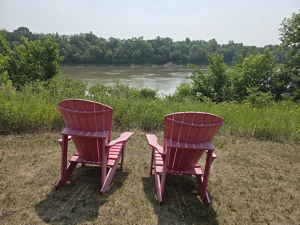 Two bright red Parks Canada chairs look across the Red River at Lower Fort Garry.