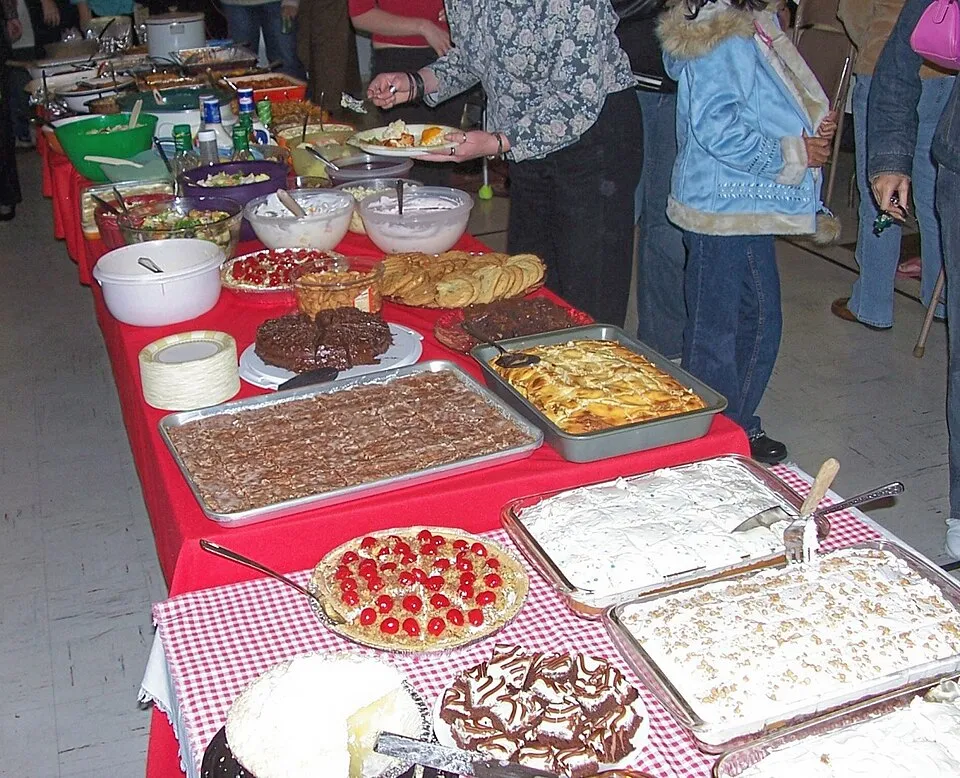 A long table holds many dishes brought to a church potluck.