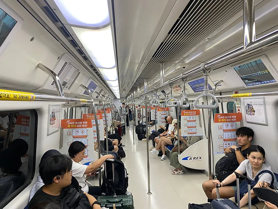 Passengers sit and stand inside a clean, modern train in the Seoul metropolitan transport system.