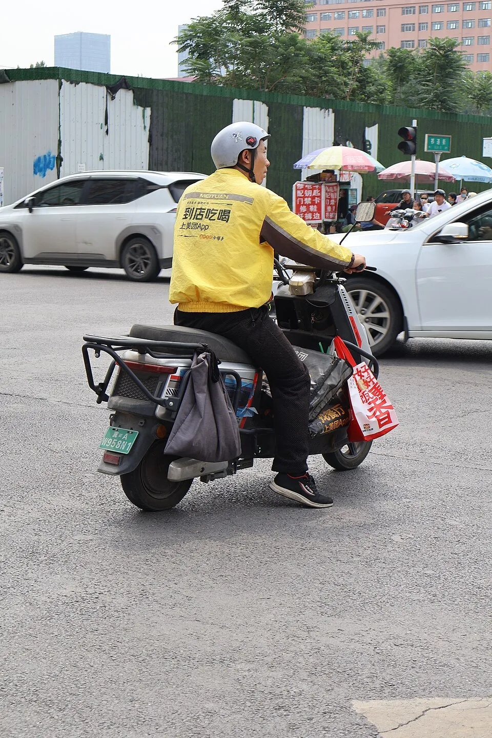 A Meituan food delivery rider travels through city traffic on a scooter in China.