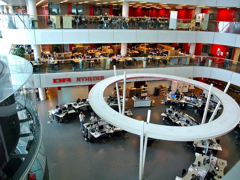 Journalists work at desks in a large television newsroom.