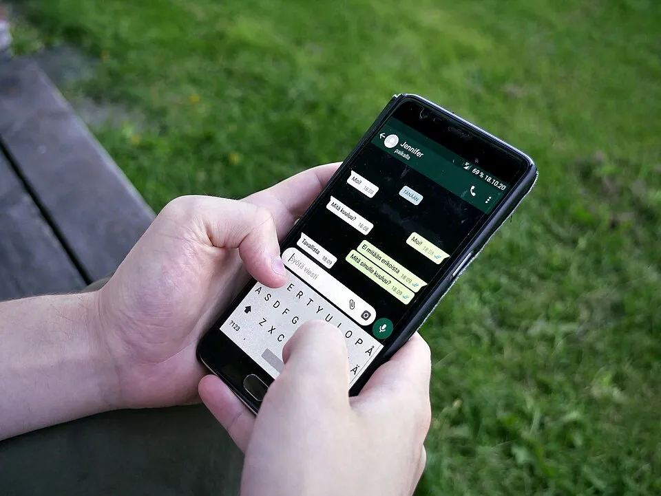 A person uses WhatsApp on a smartphone outdoors.