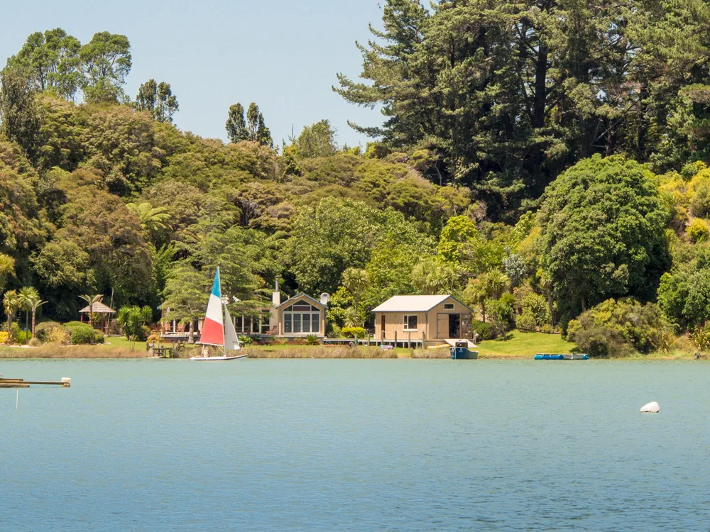 Small holiday homes stand beside calm water and green trees in New Zealand.