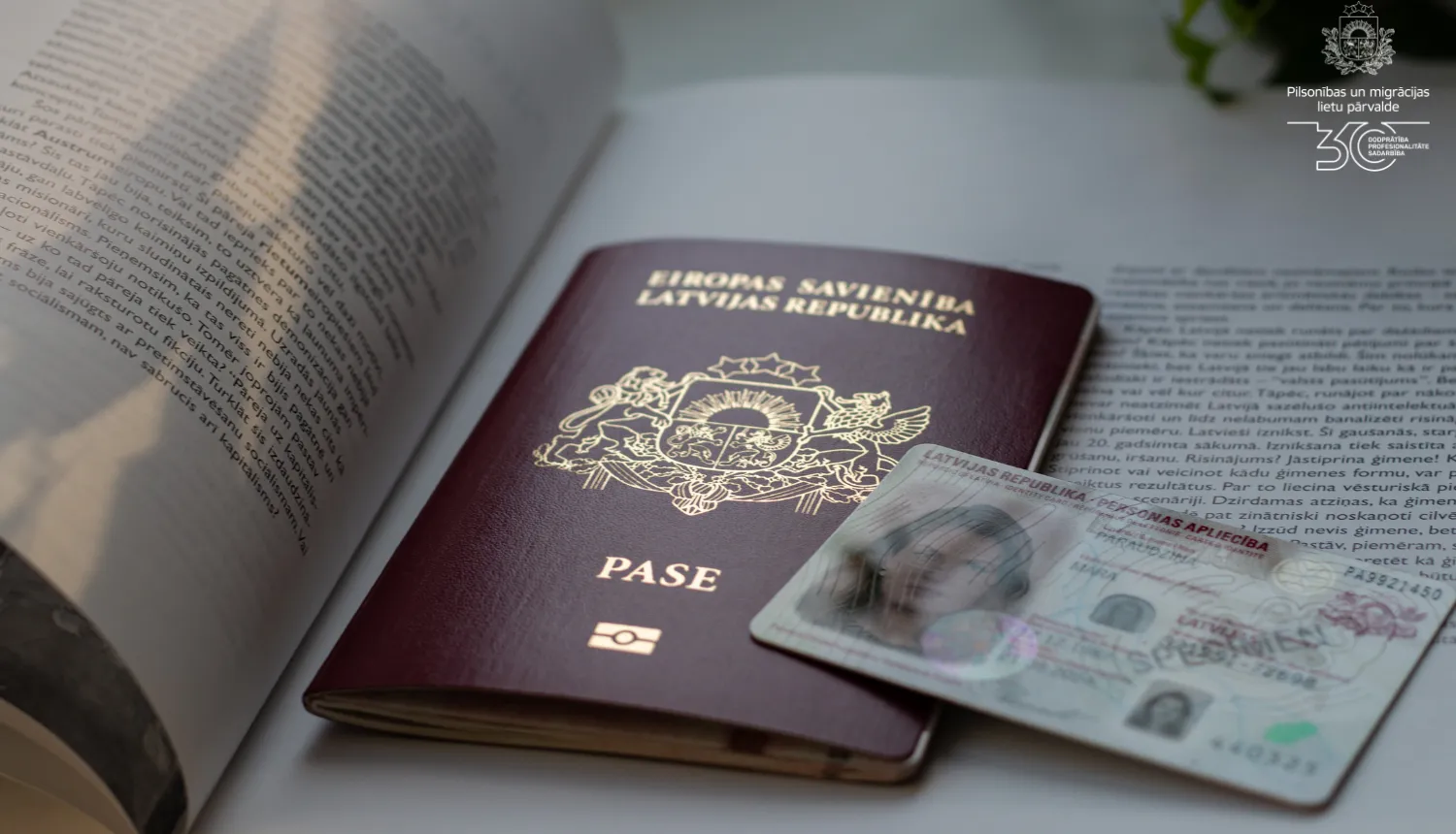 A Latvian passport and electronic identity card rest on an open book.