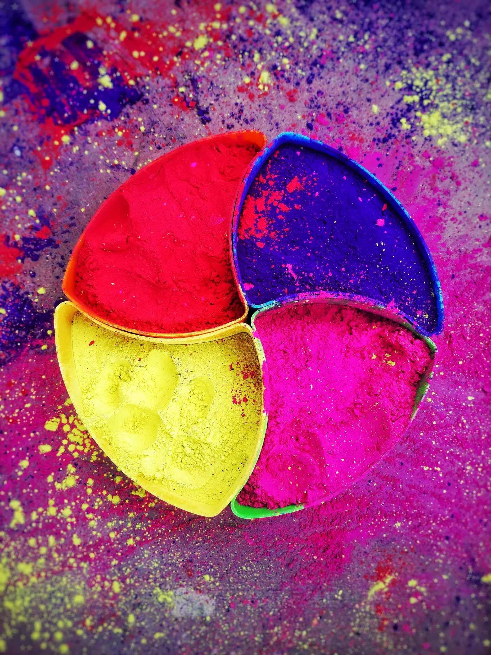 Bright Holi color powders arranged in a circle of small dishes, from red and orange to green, blue, and purple.