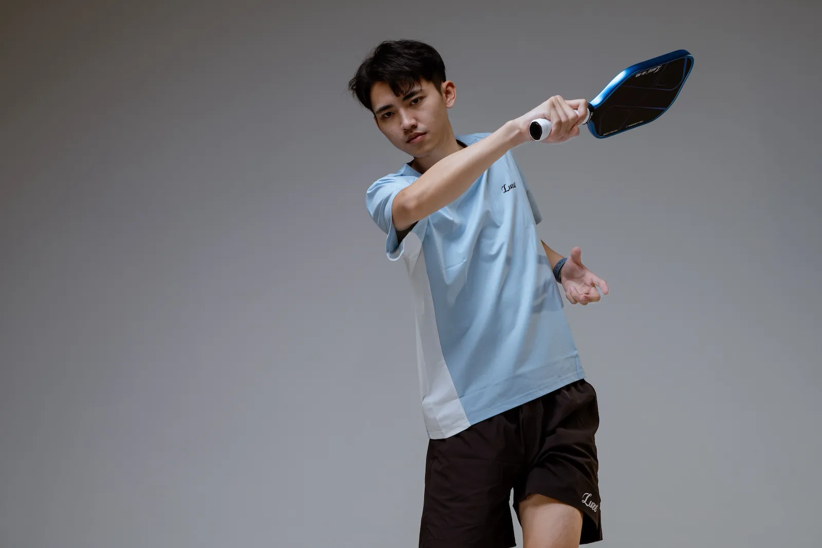 A pickleball player practises a stroke while holding a paddle on an outdoor court.